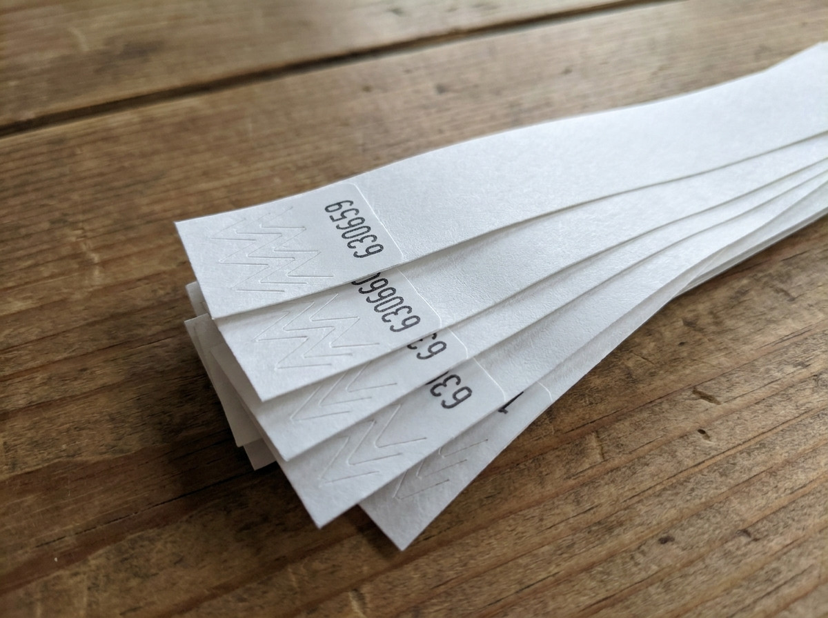 Primer plano de pulseras Tyvek con numeración secuencial impresa en negro, dispuestas en abanico sobre una mesa de control de acceso en un evento
